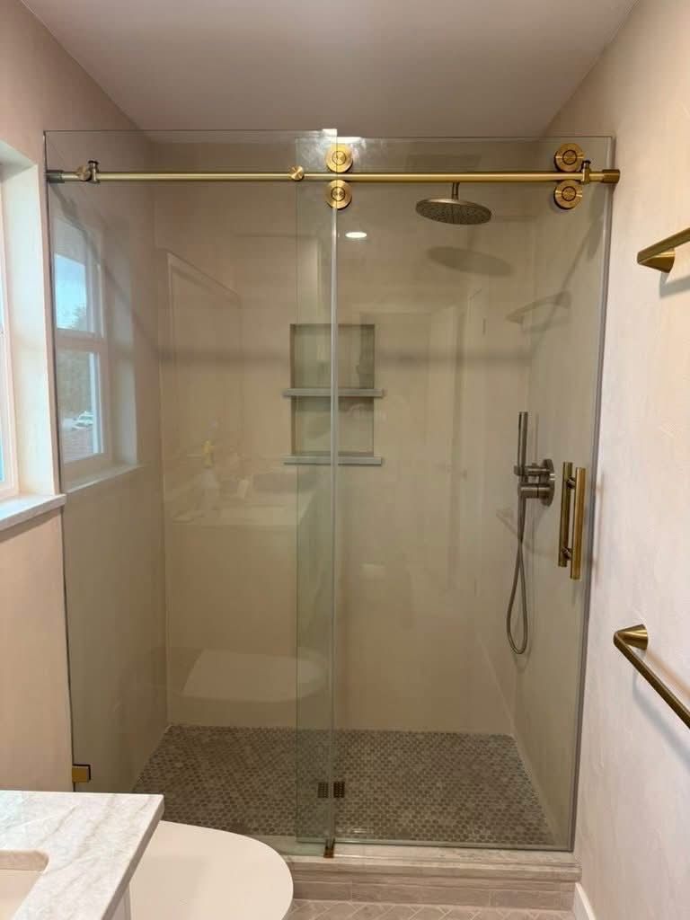 Walk-in shower with a sliding glass door on brushed brass hardware, rain showerhead and hexagon mosaic floor