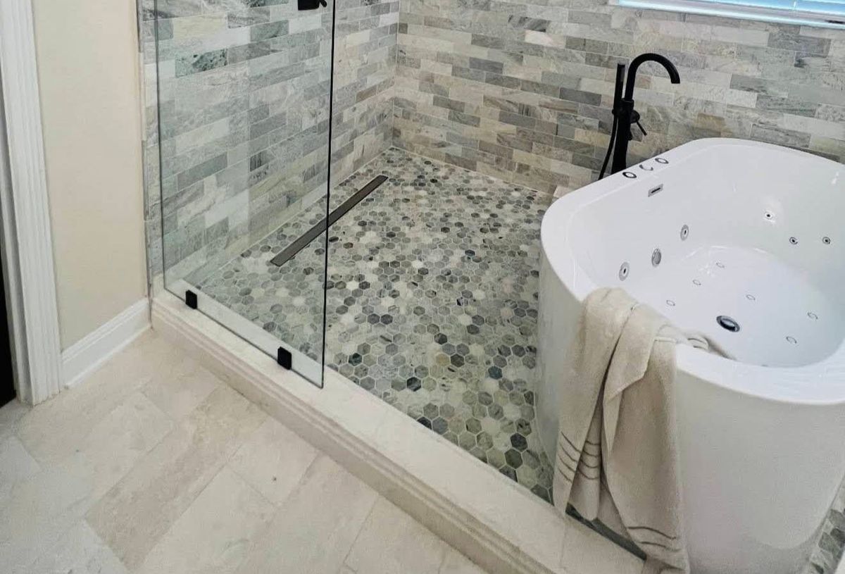 Curbless glass shower with a hexagon mosaic floor and linear drain beside a freestanding jetted tub with a matte black floor-mount faucet