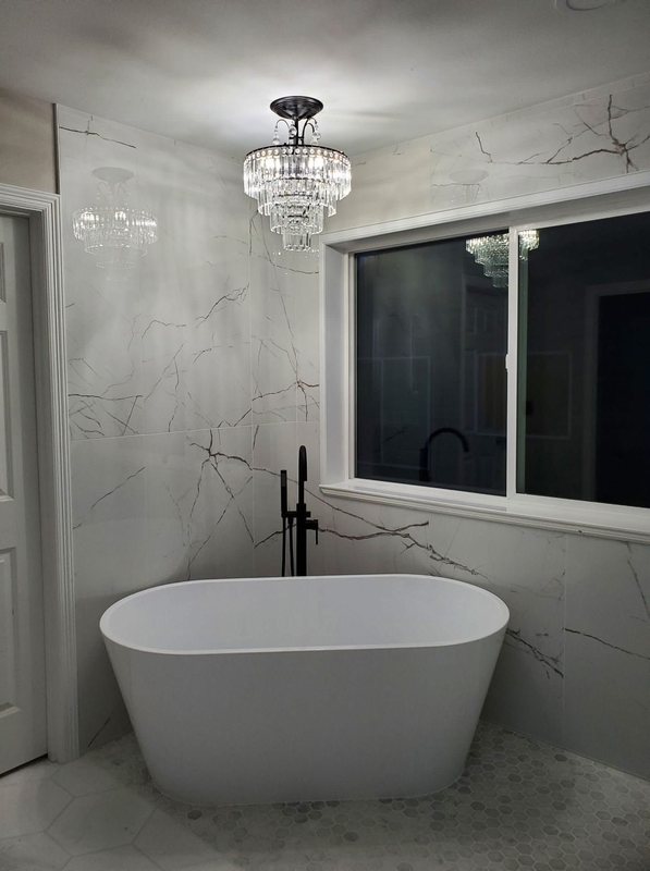 Primary bathroom with a freestanding soaking tub, crystal chandelier, marble-look tile and a glass-enclosed shower