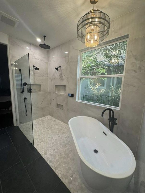 Bathroom with a glass shower enclosure, freestanding tub, chandelier and a large window