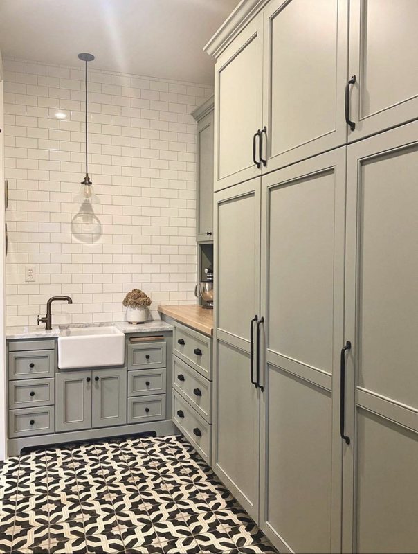 Sage green shaker cabinets with a farmhouse sink, subway tile and black-and-white patterned floor tile