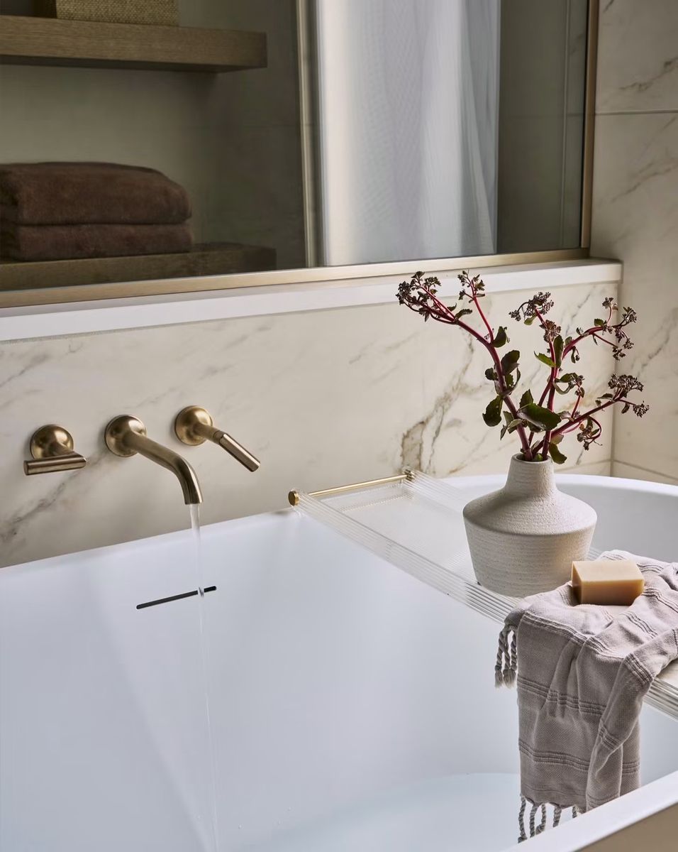Soaking tub with a brushed brass wall-mounted faucet and a marble-look tile ledge